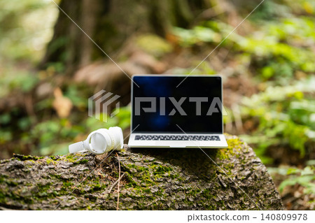 Laptop and wireless headphones placed on a tree stump in the forest 140809978