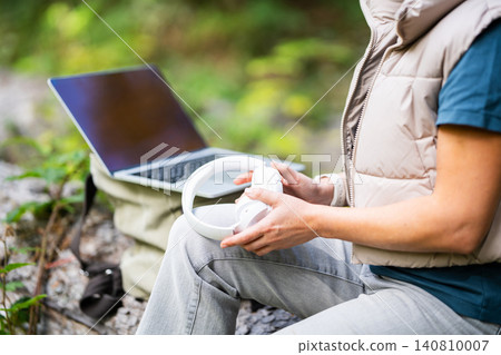 Woman with laptop and wireless headphones working in a peaceful forest Woman with laptop and wireless headphones working in a peaceful forest 140810007