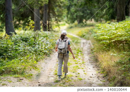 Female hiker with a backpack walking along a scenic forest road Female hiker with a backpack walking along a scenic forest road 140810044