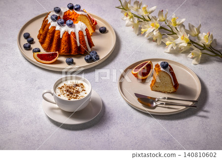 Delicious gugelhupf cake with white icing, blueberries and blood orange with cappuccino and orchid decoration Delicious gugelhupf cake with white icing, blueberries and blood orange with cappuccino and orchid decoration 140810602