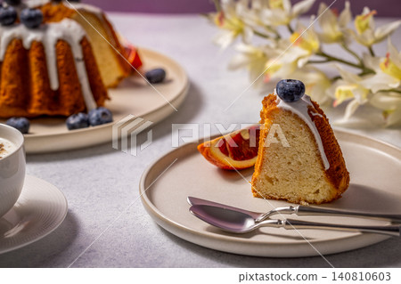 Delicious gugelhupf cake with icing, blueberries and blood orange on a plate Delicious gugelhupf cake with icing, blueberries and blood orange on a plate 140810603