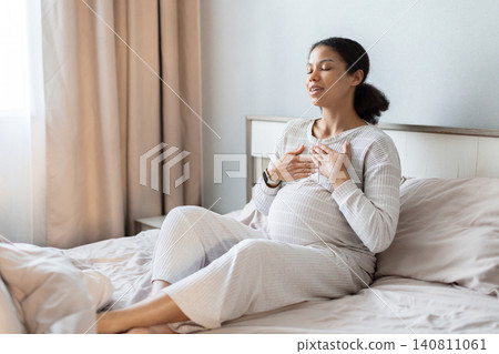 Pregnant black woman sitting on bed practicing calm breathing exercises Pregnant black woman sitting on bed practicing calm breathing exercises 140811061
