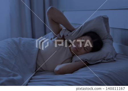 Black woman lying in bed at night covering her ear with pillow Black woman lying in bed at night covering her ear with pillow 140811167