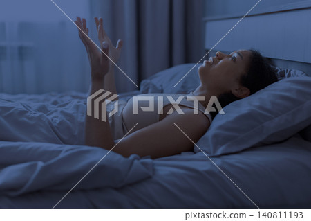 Black woman is lying awake in bed at night with raised hands Black woman is lying awake in bed at night with raised hands 140811193