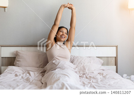 Happy black woman is stretching in bed after waking up 140811207