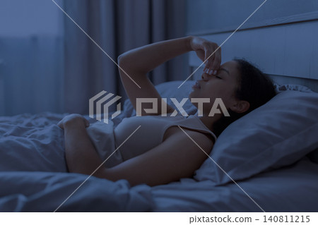 Black woman lying awake in bed at night pinching nose, suggesting sinus 140811215