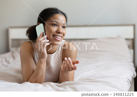 Happy black woman lying on bed while talking on smartphone 140811225