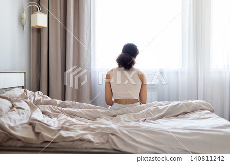 Rear view of black woman sitting on edge of bed in bedroom 140811242