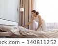 Happy African American woman making bed in bedroom, smoothing sheets and smiling 140811252