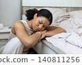 Tired black woman resting asleep beside bed with her head on folded arms 140811256