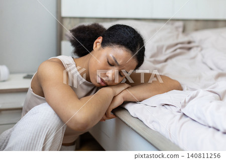 Tired black woman resting asleep beside bed with her head on folded arms 140811256