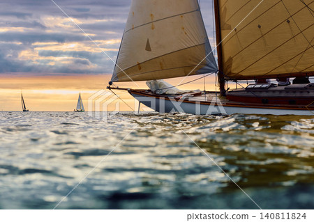 Vintage sailing boat through splashing water at sunset, Sailing regatta in the Gulf of Finland at sunset, hot race of several yachts, teamwork Vintage sailing boat through splashing water at sunset, Sailing regatta in the Gulf of Finland at sunset, hot race of several yachts, teamwork 140811824