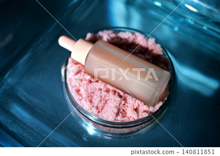 Cosmetic serum bottle resting on pink sugar scrub Cosmetic serum bottle resting on pink sugar scrub 140811851