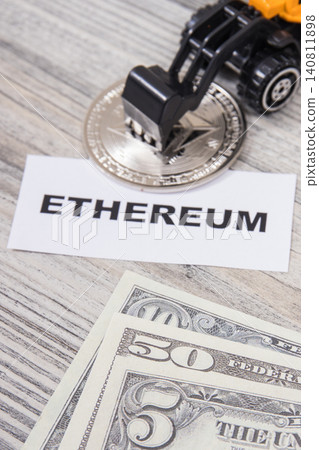 Ethereum coin, miniature excavator and dollar bills 140811898