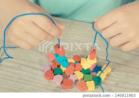 Preschooler making bracelet from thread and wooden colored beads Preschooler making bracelet from thread and wooden colored beads 140811903