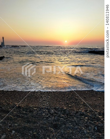 A beautiful vertical coastal landscape featuring the sunrise over the horizon and the shoreline. A beautiful vertical coastal landscape featuring the sunrise over the horizon and the shoreline. 140811946