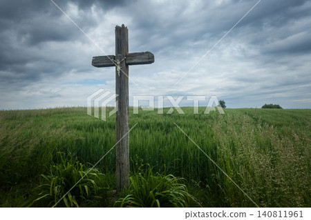 An old cross standing in a field and a cloudy sky An old cross standing in a field and a cloudy sky 140811961