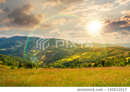 sunset over mountain landscape with grassy field. trees on the rolling hills and rural valley beneath a cloudy sky with rainbow in the background. view of carpathian mountains in summer sunset over mountain landscape with grassy field. trees on the rolling hills and rural valley beneath a cloudy sky with rainbow in the background. view of carpathian mountains in summer 140812017