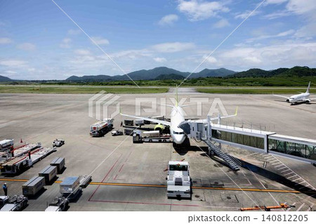 A passenger plane waiting to depart at the airport tarmac during the daytime, and ground handling operations in progress. A passenger plane waiting to depart at the airport tarmac during the daytime, and ground handling operations in progress. 140812205