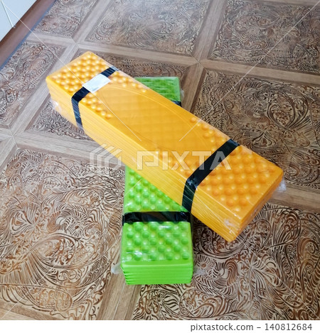 tourist mat of orange color lies on top of green mat in package on floor tourist mat of orange color lies on top of green mat in package on floor 140812684