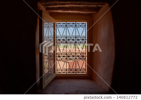 An open window with a wrought-iron grille reveals the rustic landscape of the Kasbah of Taourirt in Morocco An open window with a wrought-iron grille reveals the rustic landscape of the Kasbah of Taourirt in Morocco 140812772