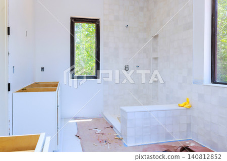 Work is ongoing in bathroom with white walls, empty cabinets, shower area waiting for fixtures. Work is ongoing in bathroom with white walls, empty cabinets, shower area waiting for fixtures. 140812852