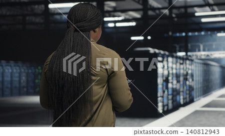Data center engineer checks server room hardware and network infrastructure with a digital device for stable operations. Data center engineer checks server room hardware and network infrastructure with a digital device for stable operations. 140812943
