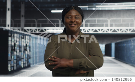 Smiling data center administrator walks through a server room while reviewing security compliance and cyber risk. Smiling data center administrator walks through a server room while reviewing security compliance and cyber risk. 140812996