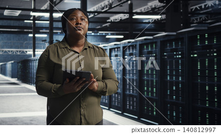 Data center engineer walks through a server room while overseeing IT infrastructure and network operations. 140812997