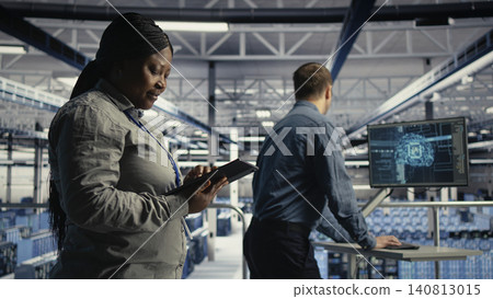 Data center employee monitors operational metrics on mockup PC inside a server room to improve infrastructure performance. 140813015