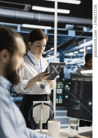 Data center engineer uses a digital tablet in a data center to manage AI virtualization and optimize server infrastructure. 140813156