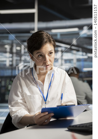 System administrator uses a clipboard in a data center to monitor equipment, manage workflows, and support reliable infrastructure. 140813157