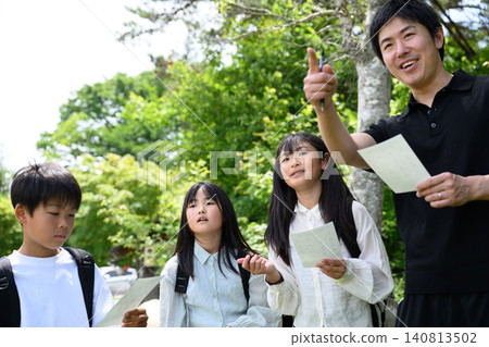 一群小學生在春天綠意盎然的戶外學習活動中認真聆聽老師的解說。 140813502