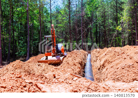 Excavator machine is digging trench in ground surrounded by trees work is for installing septic pipe 140813570