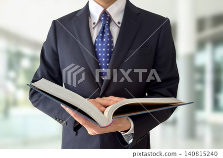 辦公室裡,一個穿著西裝的男人正在打開一本書。 辦公室裡,一個穿著西裝的男人正在打開一本書。 140815240
