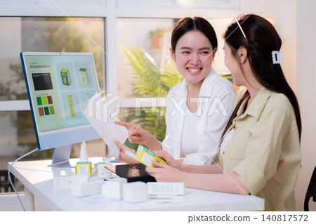 Two asian woman graphic designers analyzing product package prototype, reviewing paper sketch. Two asian woman graphic designers analyzing product package prototype, reviewing paper sketch. 140817572