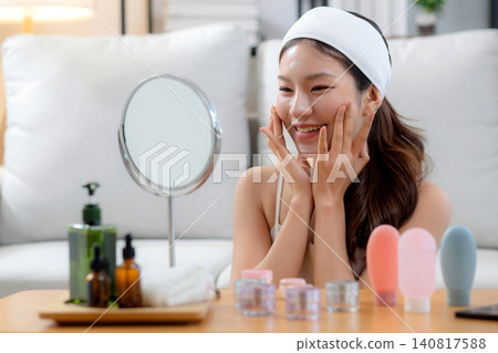 Beauty young asian woman applying cream on facial for wrinkles while looking mirror in living room. Beauty young asian woman applying cream on facial for wrinkles while looking mirror in living room. 140817588