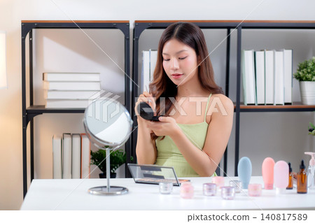 Happy young asian woman applying makeup with a brush on cheek looking mirror. Happy young asian woman applying makeup with a brush on cheek looking mirror. 140817589