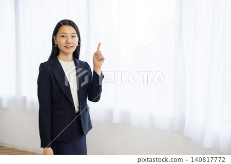 A young Japanese businesswoman holds up one index finger by the window. A young Japanese businesswoman holds up one index finger by the window. 140817772