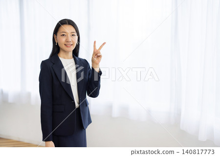 一位年輕的日本女商人站在窗邊，舉起兩根食指。 140817773