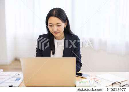 A young Japanese businesswoman working on her computer by a bright window. A young Japanese businesswoman working on her computer by a bright window. 140818077