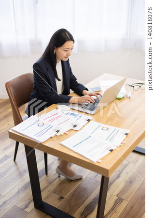 A young Japanese businesswoman working on her computer by a bright window. A young Japanese businesswoman working on her computer by a bright window. 140818078