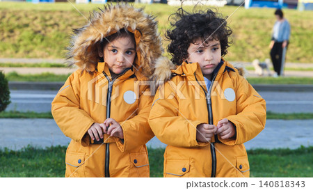 Young siblings wearing warm matching yellow parkas with fur hoods outdoors Young siblings wearing warm matching yellow parkas with fur hoods outdoors 140818343