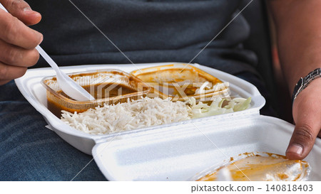 Enjoying Indian street food meal with rice and curry in a takeaway container Enjoying Indian street food meal with rice and curry in a takeaway container 140818403
