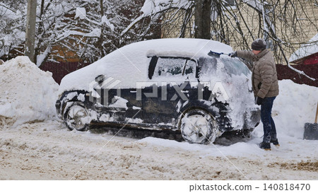 Man scraping snow from car in harsh winter conditions during a blizzard Man scraping snow from car in harsh winter conditions during a blizzard 140818470
