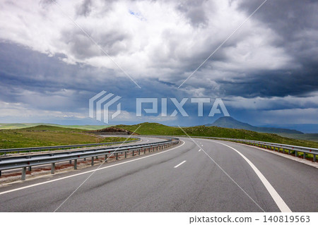 Winding highway stretches over grassy terrain beneath storm clouds Winding highway stretches over grassy terrain beneath storm clouds 140819563