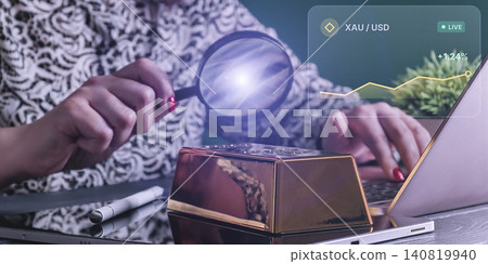 Commodities trading concept: Woman analyzing a gold bar and live XAU/USD market chart near a laptop Commodities trading concept: Woman analyzing a gold bar and live XAU/USD market chart near a laptop 140819940