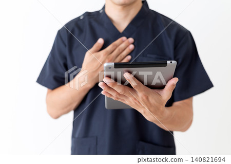 一位身穿藏藍色手術服的中年男醫生拿著平板電腦,將手放在胸前。 一位身穿藏藍色手術服的中年男醫生拿著平板電腦,將手放在胸前。 140821694