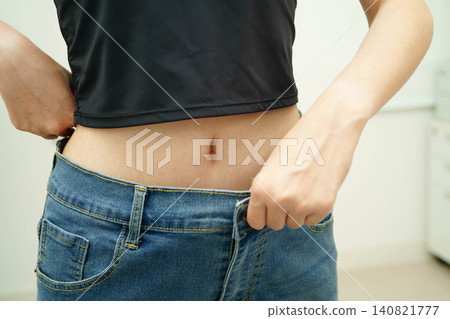 Young Asian woman losing weight wearing loose pants in oversize jeans. Young Asian woman losing weight wearing loose pants in oversize jeans. 140821777