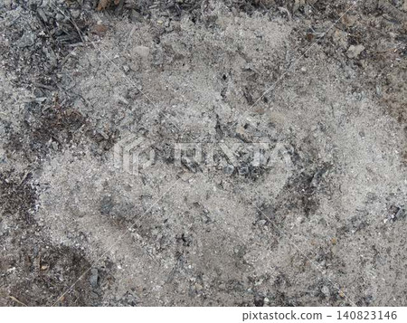 The texture of cooled wood ash after a campfire. The gray powdery mass is mixed with small black embers and pieces of charred branches, creating an uneven, rough surface. The texture of cooled wood ash after a campfire. The gray powdery mass is mixed with small black embers and pieces of charred branches, creating an uneven, rough surface. 140823146